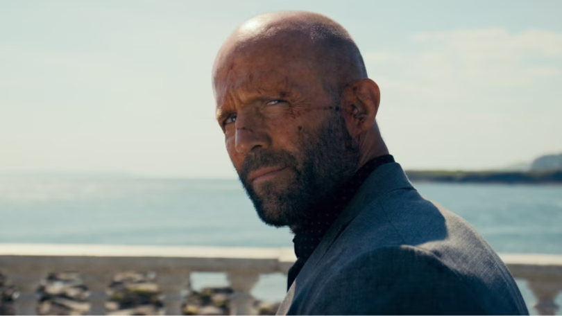 jason statham as adam clay with his face bloodied looking back with a small smile in the beekeeper.j